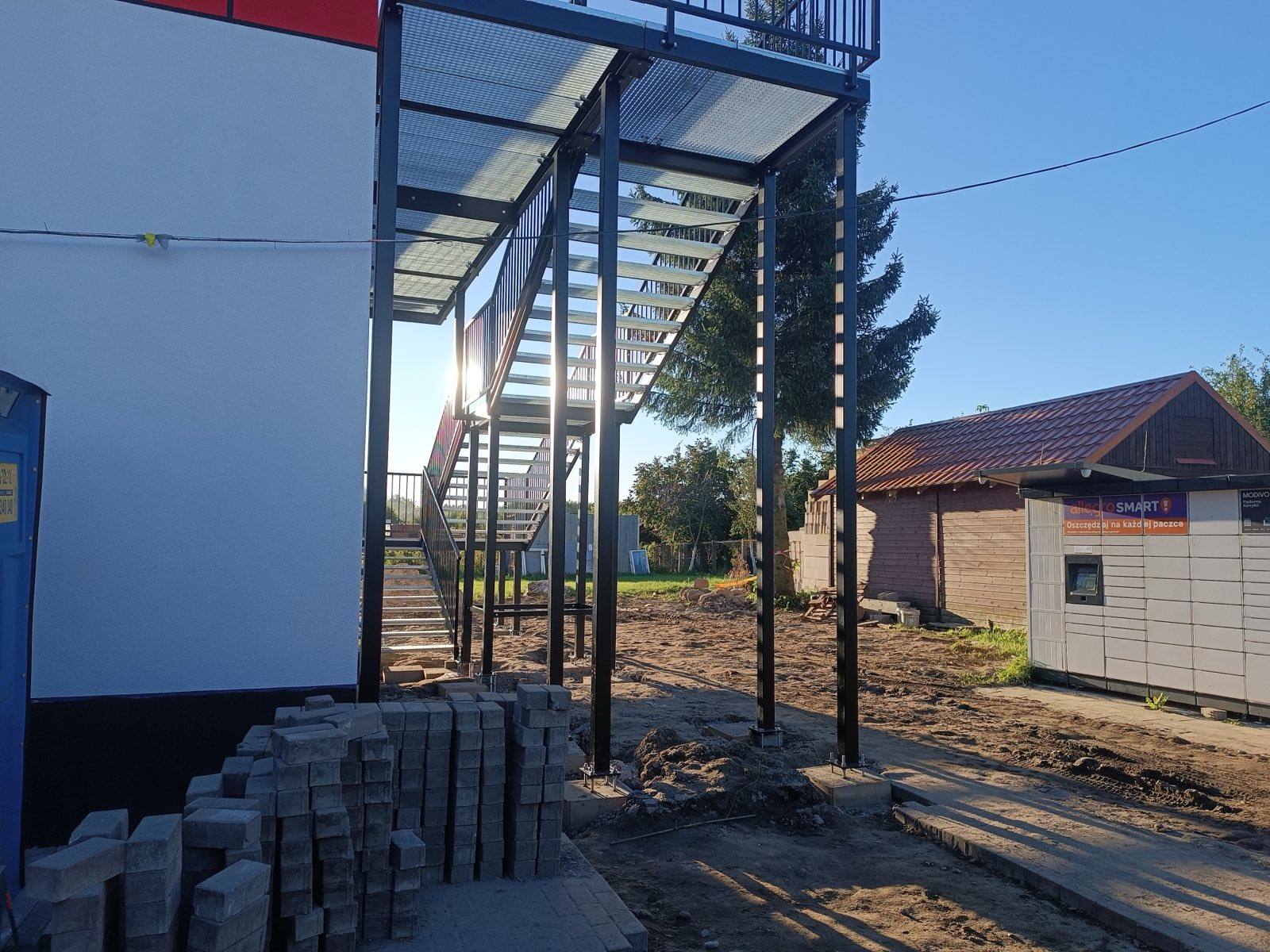 Zewnętrzna stalowa klatka schodowa przy budynku OSP Łęcze — konstrukcja stalowa i układanie kostki brukowej